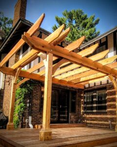 A custom wooden pergola attached to a brick house, providing shade for a deck, built by Minnesota Pergolas in Lakeland, MN.