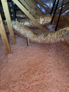 Pink blown-in insulation in an attic with a depth ruler, installed by Gulf Coast Spray Foam Insulation & Coatings, LLC in Mobile, AL