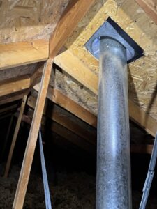 An attic showing a metal flue pipe and existing insulation, inspected by Pacific Insulation & Mold Remediation in Spokane, WA.
