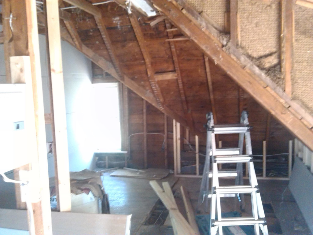 An attic space with exposed wooden framing, insulation, and a ladder, indicating renovation work by Sanow Construction in Huron, SD.