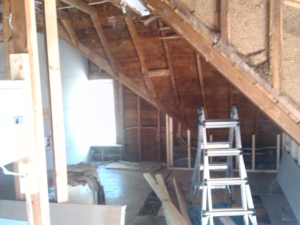An attic space with exposed wooden framing, insulation, and a ladder, indicating renovation work by Sanow Construction in Huron, SD.