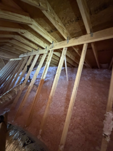 A wide view of an attic space with new pink blown-in insulation and wooden rafters from Gulf Coast Spray Foam Insulation & Coatings, LLC in Mobile, AL