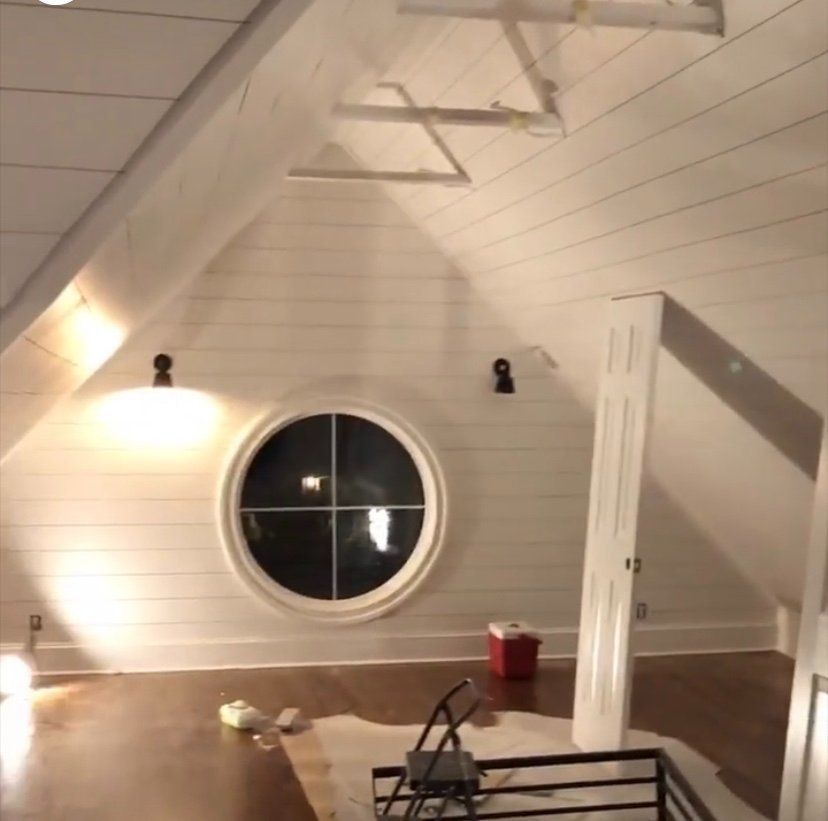 An attic space undergoing renovation with newly installed shiplap walls and a unique round window by Dogwood Renovation & Design, LLC in Kansas City, MO.