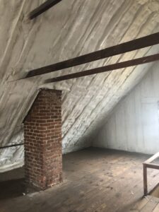 Attic space with spray foam insulation applied to roof rafters and around a brick chimney by Spray Foam Art-Insulation in Stamford, CT.