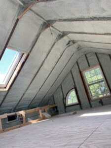 An attic space with spray foam insulation applied to the roofline and walls, featuring skylights, by Metro Insulation in Rockford, IL.