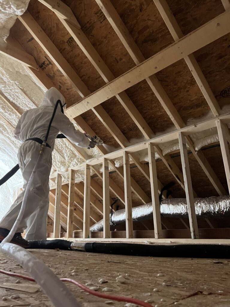 A worker applying spray foam insulation to the attic roof framing for Off-Axis Spray Foam and Radon Services in Clarksville, TN.