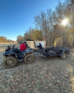 An ATV pulling a trailer full of old tires towards a dumpster for junk removal by Curry Dumpster Rentals LLC in Southaven, MS.