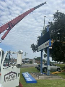 A B & H Metal Buildings Inc. crane truck lifting a sign component for installation in Kenner, LA.
