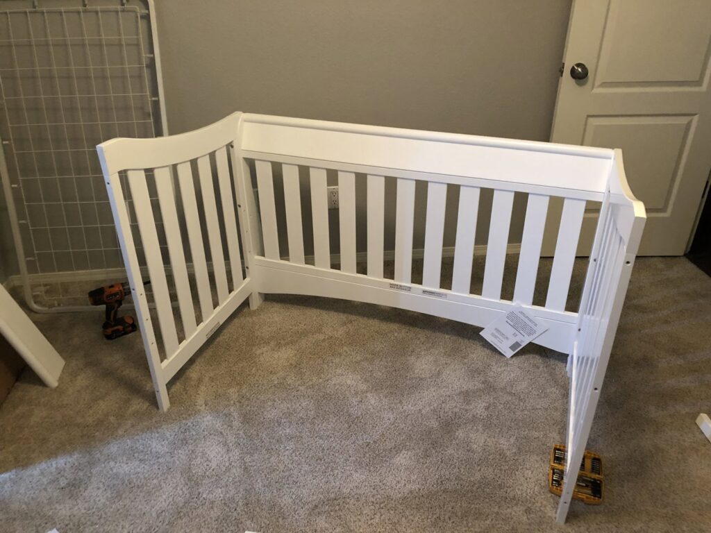 A white baby crib side panel being assembled, with a drill and tools on the carpet, demonstrating furniture assembly by The ABQ Handyman in Albuquerque, NM.