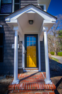 The back exterior of a house with dark siding, white trim, a deck, and stairs, expertly maintained by Boston Exterior Remodeling in Boston, MA.