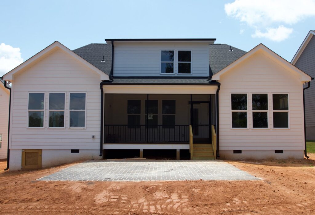 The back of a modern house featuring a newly installed screened porch and a paved patio area by Screen Enc in Denver, NC