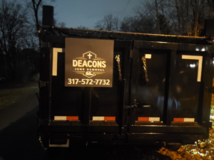 The back of a black junk removal dump trailer, branded with the business logo for Deacons Junk Removal & Recycling in Carmel, IN.