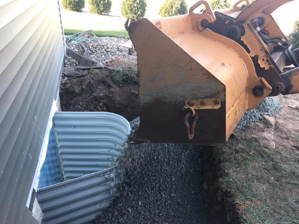 A backhoe filling gravel into an egress window well by Al Dorn Construction in De Pere, WI.