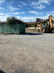A backhoe loading tree branches and construction debris into a roll-off dumpster for A Track-Out Solution in Las Vegas, NV.