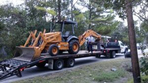 A backhoe loaded on a trailer for transport by All Aboard Contractors in Houston, TX.