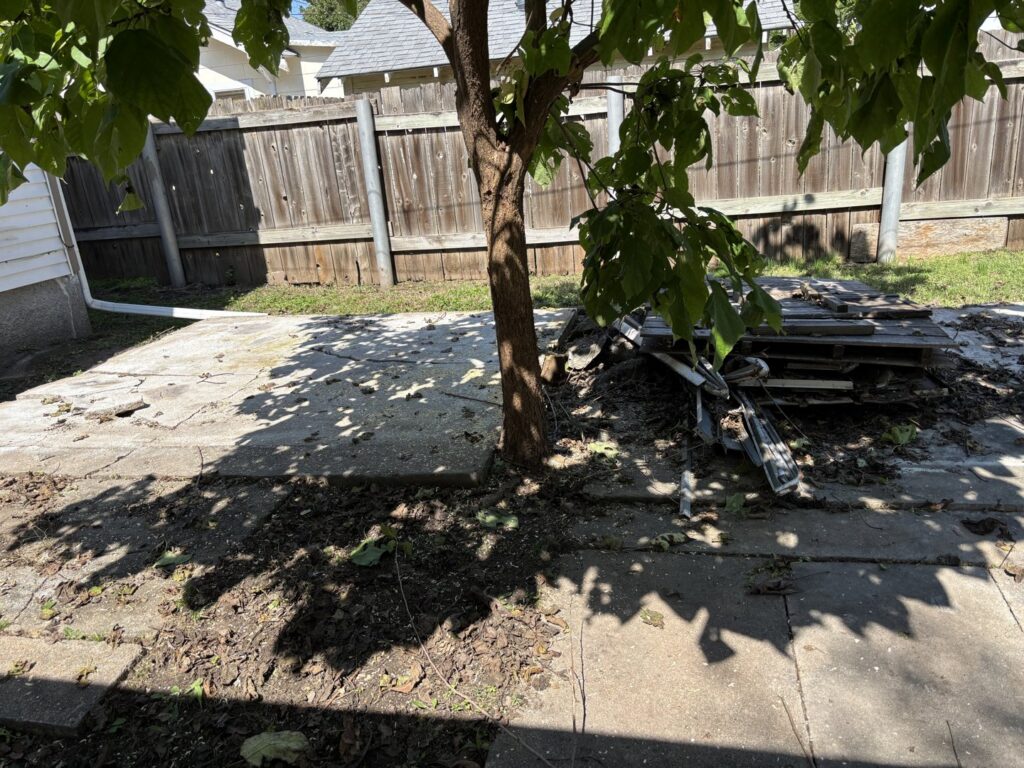 A backyard with a concrete patio and debris, including pallets and wood, ready for removal in Wichita, KS.