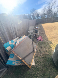 Discarded cardboard boxes and old patio furniture piled in a backyard, awaiting removal by JD Junk Removal in Raleigh, NC.