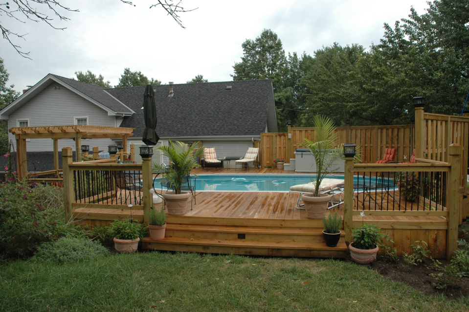 A beautifully constructed backyard deck with a swimming pool and wooden fence by Holm Remodeling Company in Kansas City, KS.