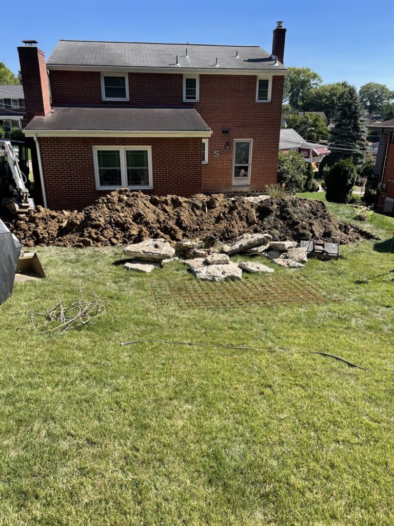 A backyard excavation project with a large pile of dirt and rocks by Integrated Contracting and Renovations in Pittsburgh, PA.