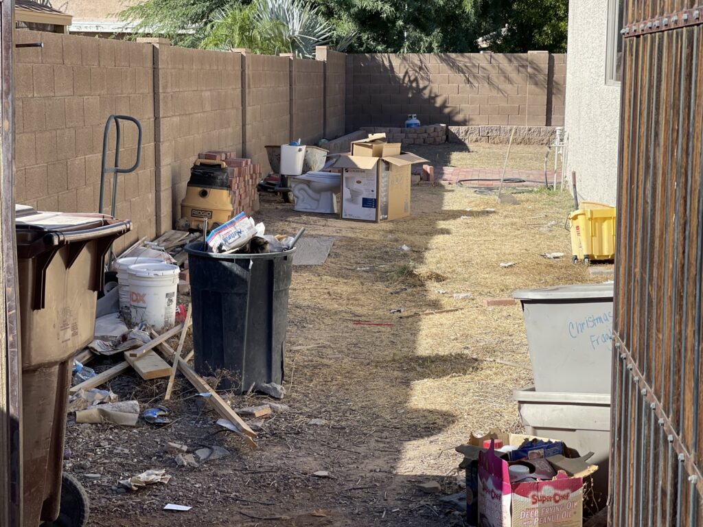 A backyard filled with various junk, trash cans, and debris, ready for removal by Canyon State Junk Removal in Peoria, AZ