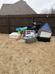 A large pile of assorted junk including a small boat, coolers, and trash bags in a backyard, ready for removal by MOAT's Junk Removal LLC in Jonesboro, AR.