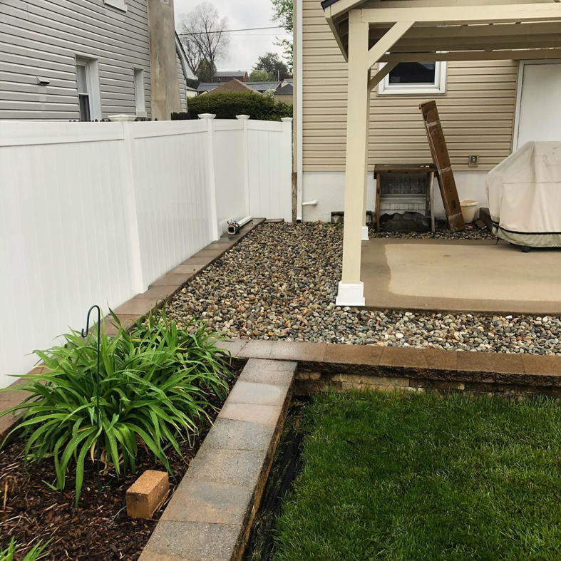 A backyard with new white fencing, stone landscaping, and a patio installed by Imagine It Home Improvements Co. in Bethlehem, PA.