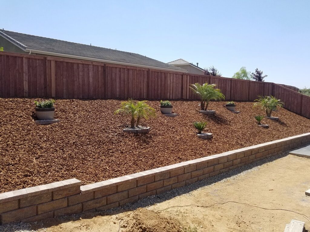 A newly landscaped backyard featuring a retaining wall, mulch, and plants by Bakoboy Enterprise Inc in Bakersfield, CA.