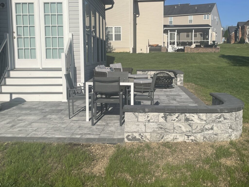 A backyard paver patio with a stone retaining wall and outdoor furniture, completed by Landscape By Today in Bowie, MD.