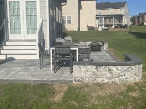 A backyard paver patio with a stone retaining wall and outdoor furniture, completed by Landscape By Today in Bowie, MD.