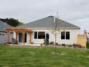 A backyard featuring a newly installed wooden pergola attached to a house and a wooden fence by Minnesota Pergolas in Lakeland, MN.