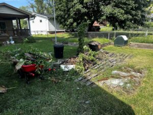A backyard with a large pile of branches, wood, and other yard waste, with a red wheelbarrow, indicating a junk removal job by Junk-O-Haulics in Westmoreland, TN.