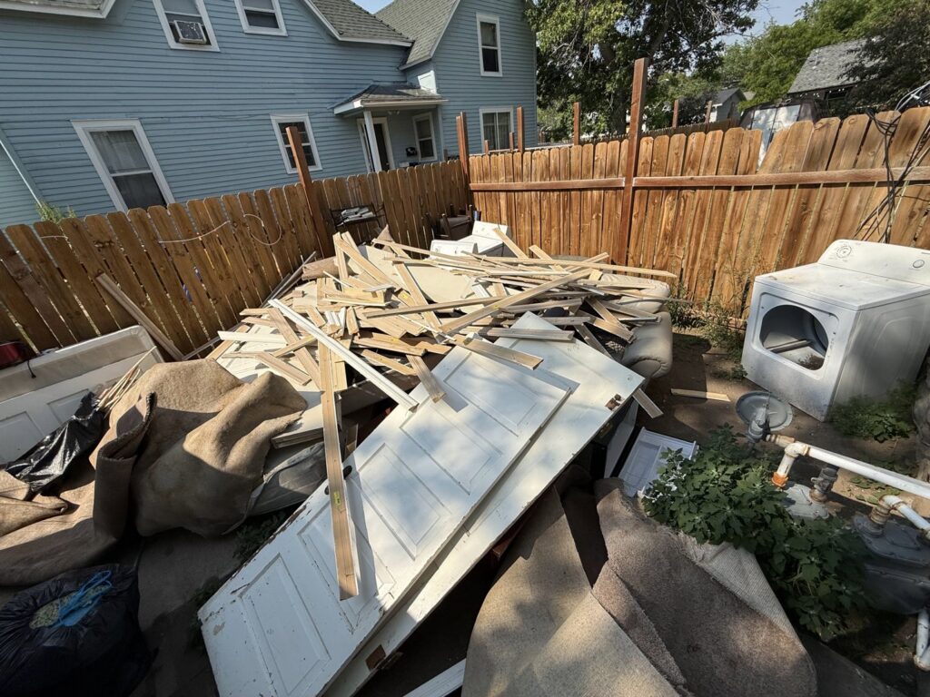 A large pile of wood, doors, and construction debris in a backyard, ready for removal by Hudson's Trash Removal, LLC in Great Falls, MT.