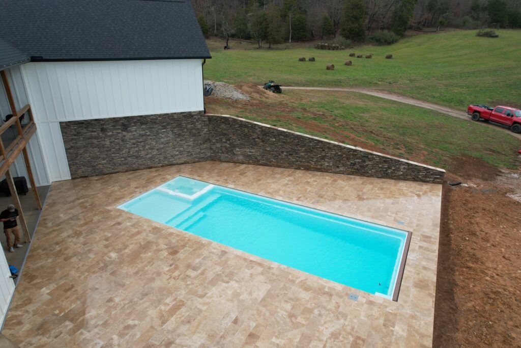 A backyard pool with a sturdy stone retaining wall and elegant patio, constructed by Southern Pool Solutions in Knoxville, TN.
