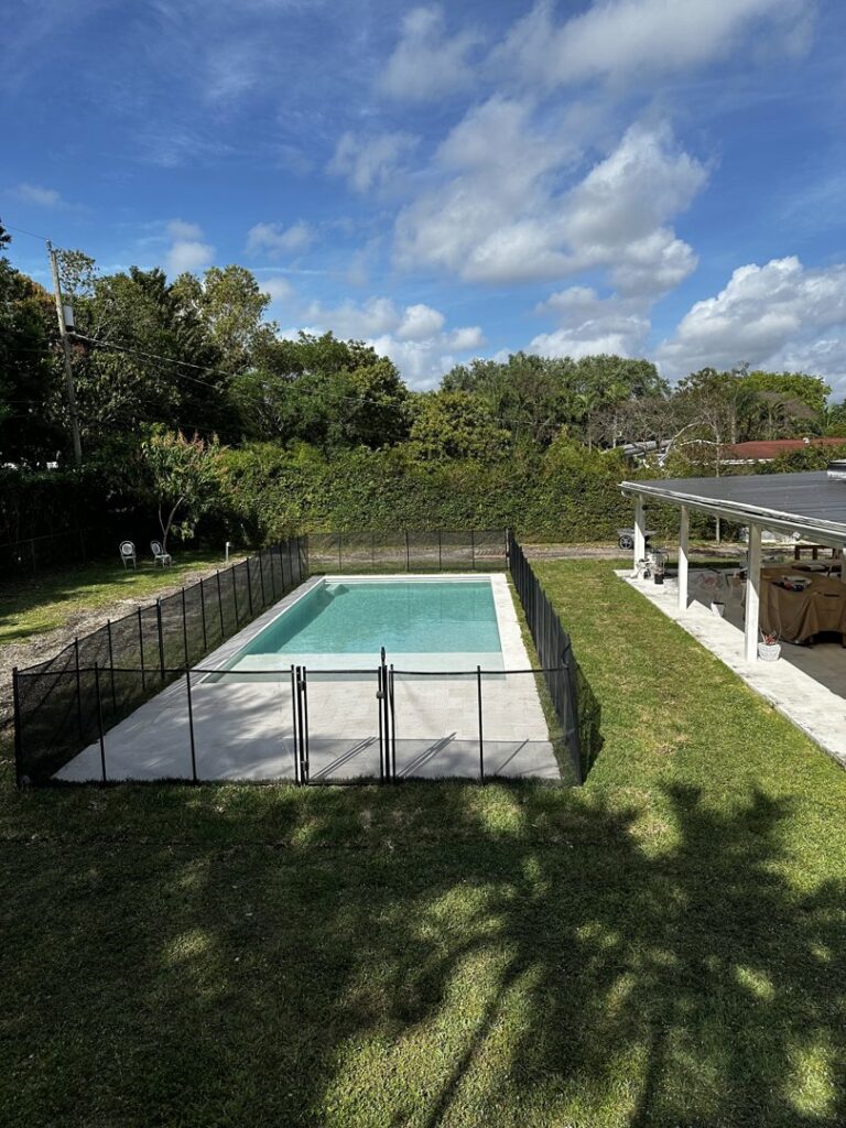 A newly installed backyard swimming pool surrounded by a black safety fence, completed by BAFCO POOLS in Hialeah, FL.