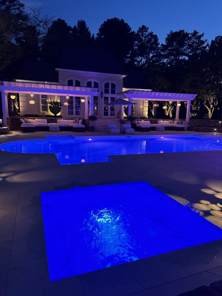 An illuminated backyard swimming pool and spa at night, showcasing outdoor lighting by Picasso Poolscapes in Johns Creek, GA.