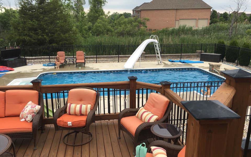 A residential backyard pool featuring a slide and a wooden deck, installed by Heatwave Pools LLC in Flint, MI.