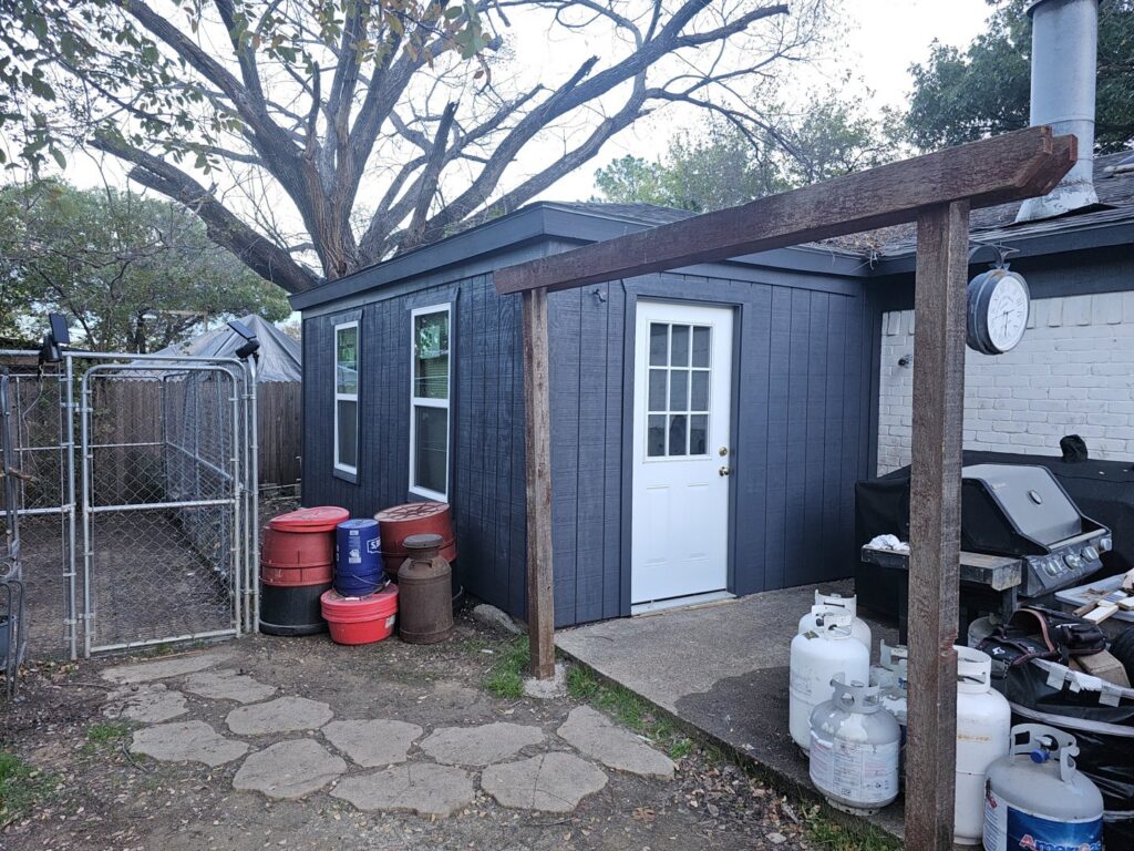 A newly constructed backyard shed or extension with dark siding and a white door, built by M.M. Remodelers in Resaca, GA.