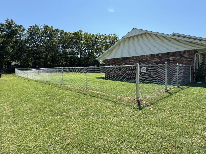A newly installed silver chain-link fence enclosing a residential backyard by Herron Fencing LLC in Shawnee, OK.