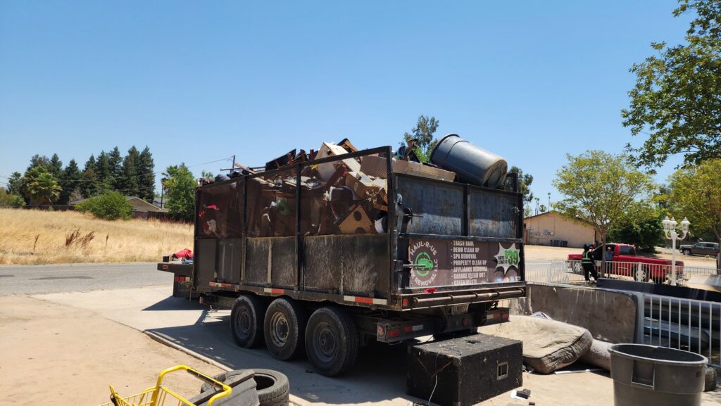 A cluttered backyard filled with old tires, a lawnmower, and various junk, ready for removal by Haul-R-Us Junk Removal LLC in Fresno, CA.