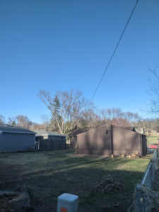 A backyard showing a tree stump and piles of branches and wood debris after tree service by S.O.S tree service in Sioux City, IA.