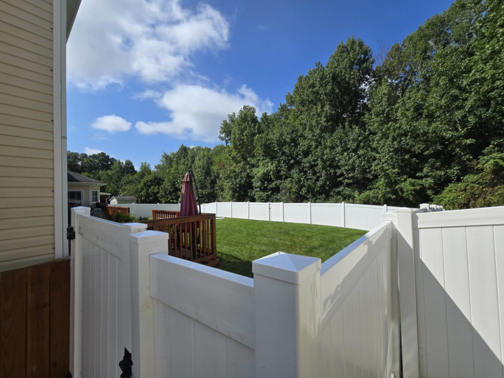 A backyard view showcasing a newly installed white vinyl fence and gate by S&L Decking and Fencing in Charlotte, NC.