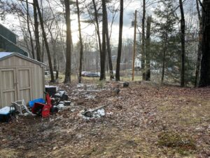 A backyard with scattered debris, fallen branches, and junk items, ready for cleanout by Tj's junk removal LLC in Derry, NH.