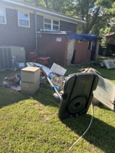 A backyard filled with large junk items and debris, including a basketball hoop and cabinet, for removal by LP Junk Removal in Birmingham, AL.