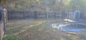 A backyard view with a retaining wall and visible tree stumps on the hillside, showing tree removal work by Hemlock Tree Service in Sioux City, IA