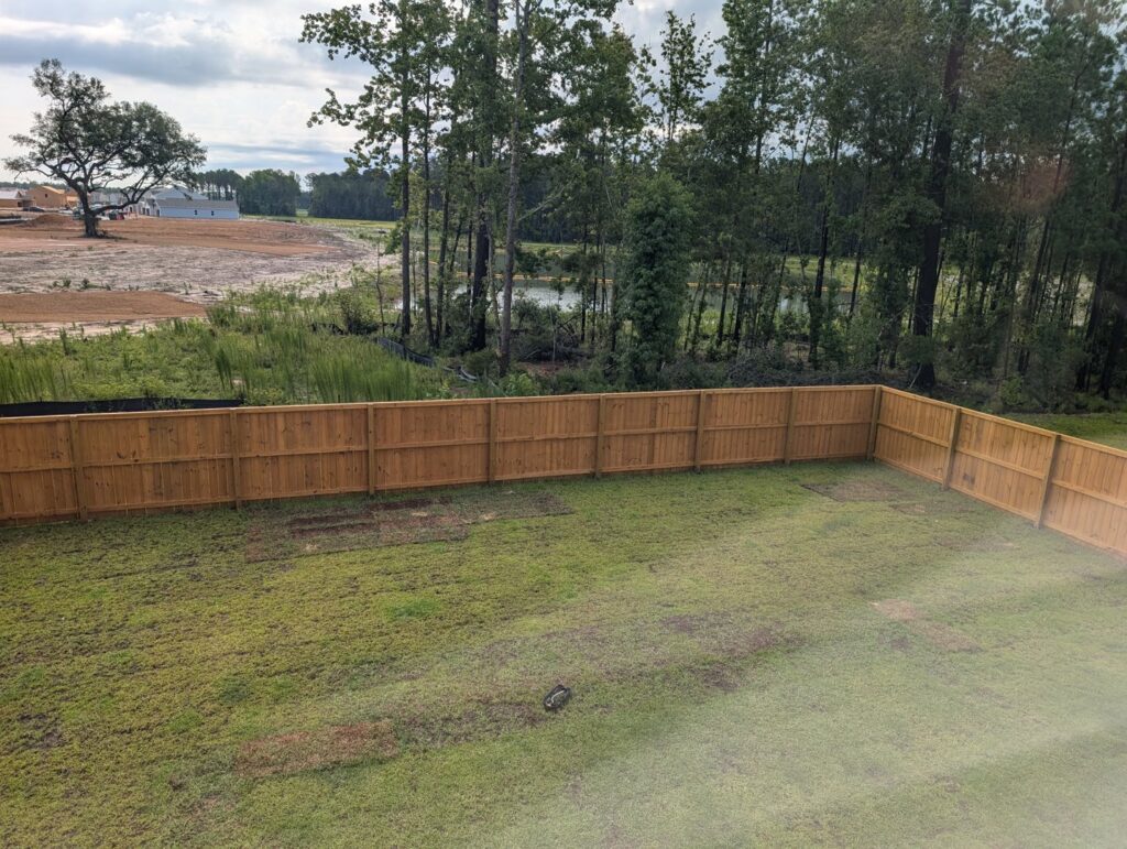 A long wooden privacy fence enclosing a backyard with a scenic pond and trees, installed by Frontline Fencing LLC in Summerville, SC.