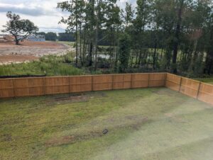 A long wooden privacy fence enclosing a backyard with a scenic pond and trees, installed by Frontline Fencing LLC in Summerville, SC.