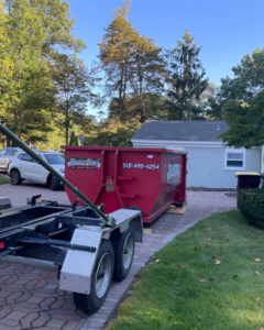 A Bada Bin junk removal dumpster being picked up or delivered by a truck on a paved driveway in Schenectady, NY.