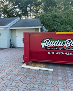 A Bada Bin dumpster rental placed on a paved driveway in front of a garage for junk removal in Schenectady, NY.