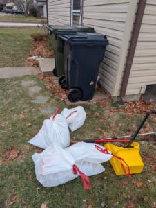 Several white bags of dog waste and a yellow scoop tool ready for disposal by BM'S Dog Poop Removal in Livonia, MI.