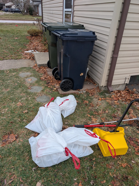 Several white bags of dog waste and a yellow scoop tool ready for disposal by BM'S Dog Poop Removal in Livonia, MI.